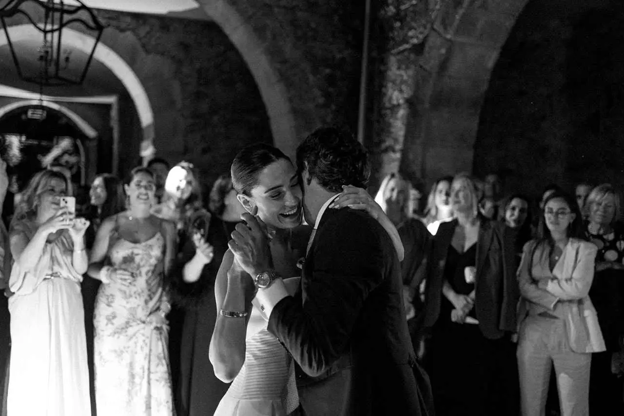Los novios bailan abrazados ante los invitados, bajo los arcos de piedra, en blanco y negro