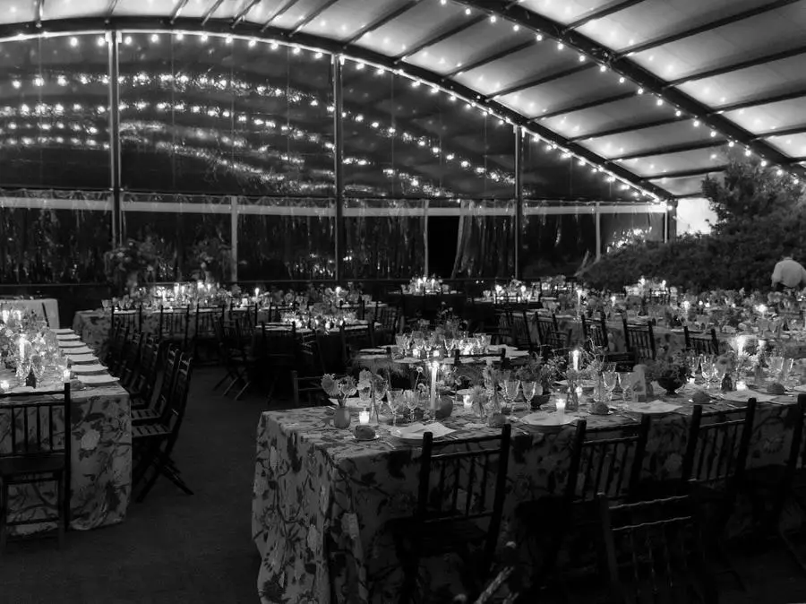 La carpa iluminada con guirnaldas de luces sobre las mesas puestas para la cena, en blanco y negro
