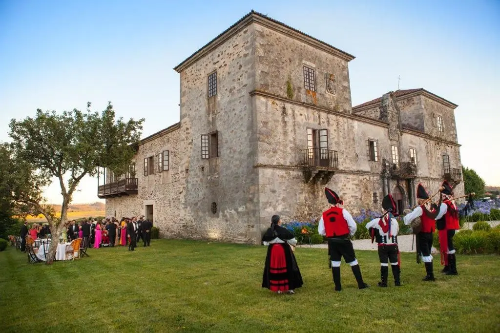 Un grupo en traje tradicional actúa en el césped ante los invitados, con el pazo detrás a última hora de la tarde