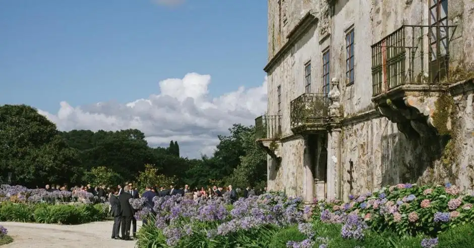 Invitados junto a la fachada del pazo, entre hortensias y agapantos, bajo un cielo con nubes